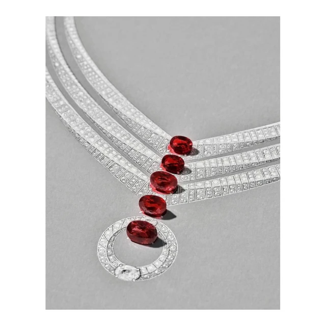 Close-up studio shot of a diamond necklace with red gemstones on a gray surface. Jewelry advertisement for the fashion industry.