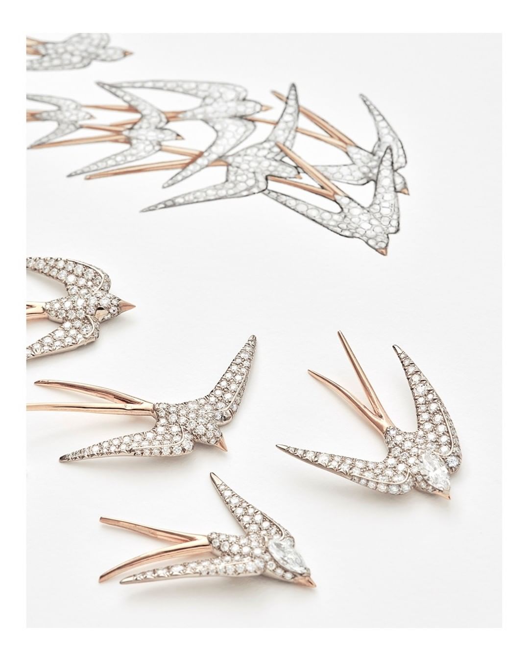 Close-up of several swallow-shaped brooches with silver bodies and gold wings scattered on a white surface, studio lighting.