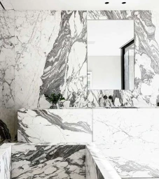 Luxurious bathroom interior featuring dramatic white and grey veined marble walls and a rectangular wall-mounted mirror.
