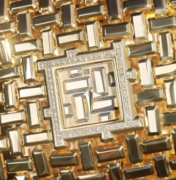 Close-up macro shot of a luxury gold watch face encrusted with square-cut diamonds and geometric gold links.