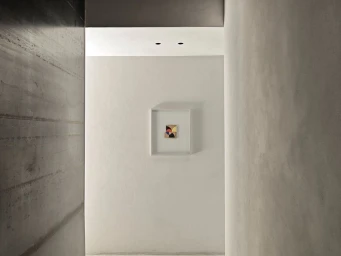Minimalist architectural interior view featuring a small framed geometric artwork mounted on a central white wall.