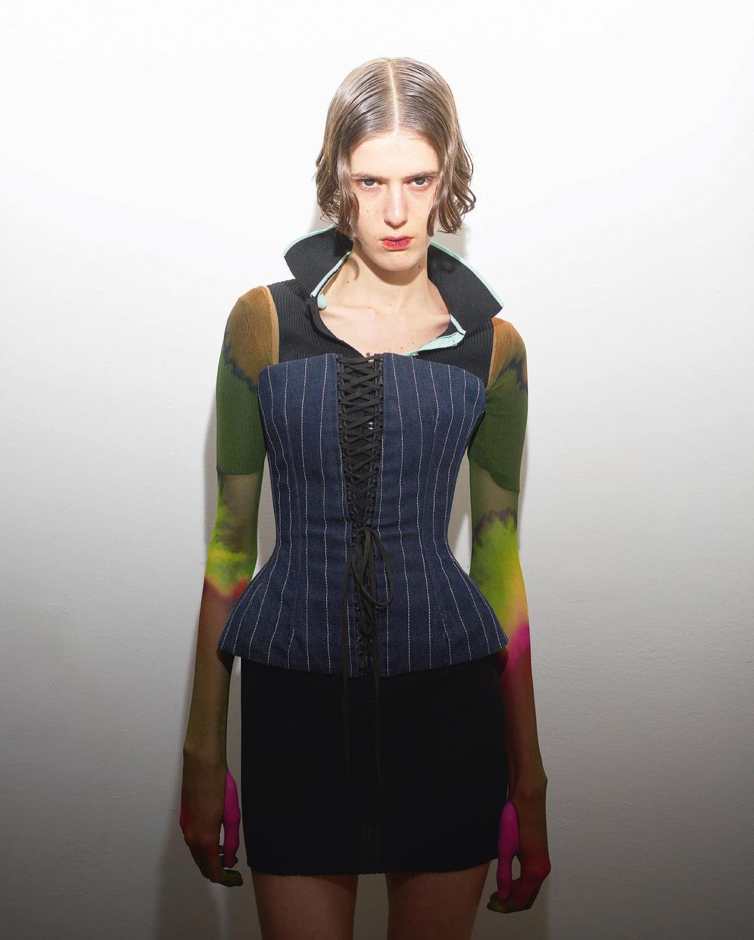 Female fashion model posing in a corset top and black mini skirt in a photo studio with a neutral background for editorial content.