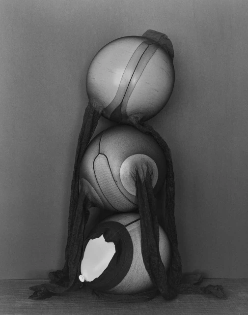 Three balloons covered in pantyhose, stacked vertically on top of each other, set against a grey background in a studio photograph.