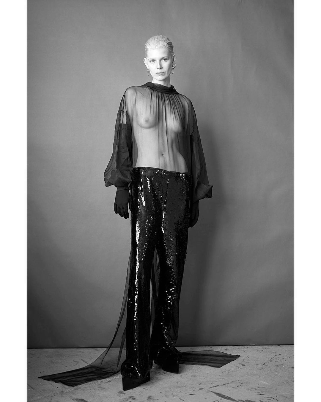 Black and white fashion shot featuring a slender adult female with fair skin, silver hair, and dramatic dark, shimmering pants.