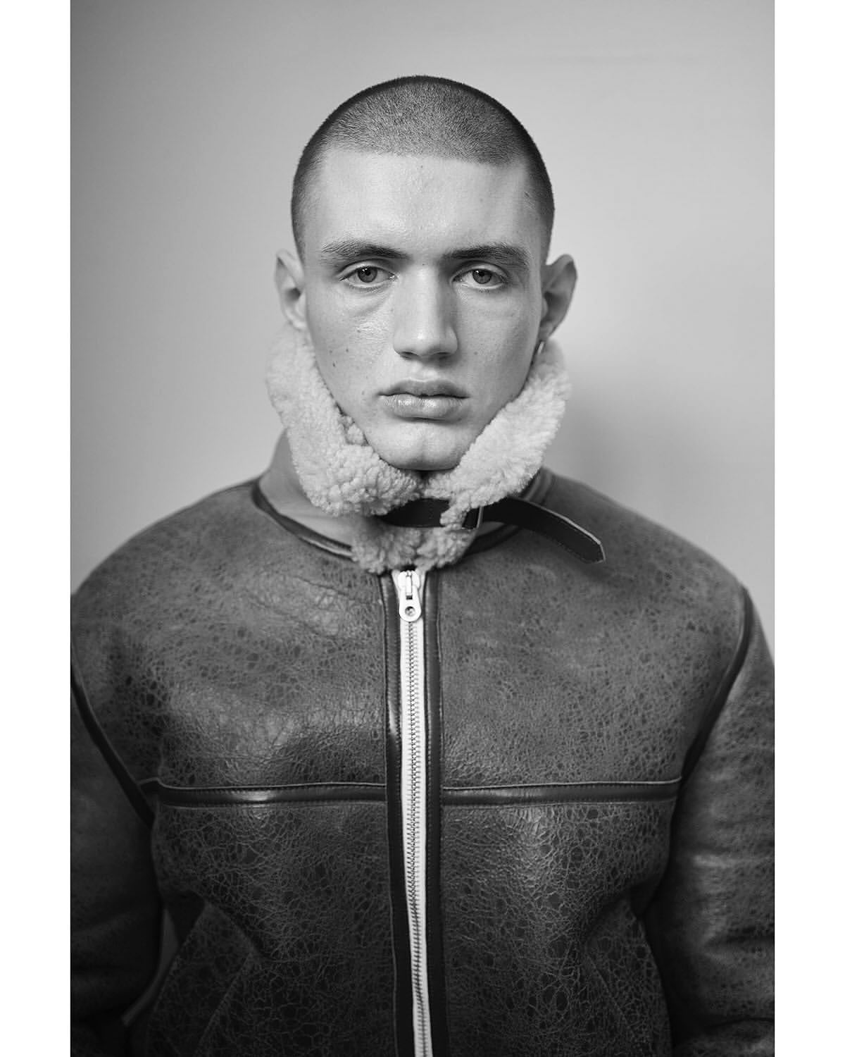 Black and white portrait of a young adult man wearing a shearling-lined bomber jacket, showcasing fashion and portrait photography.