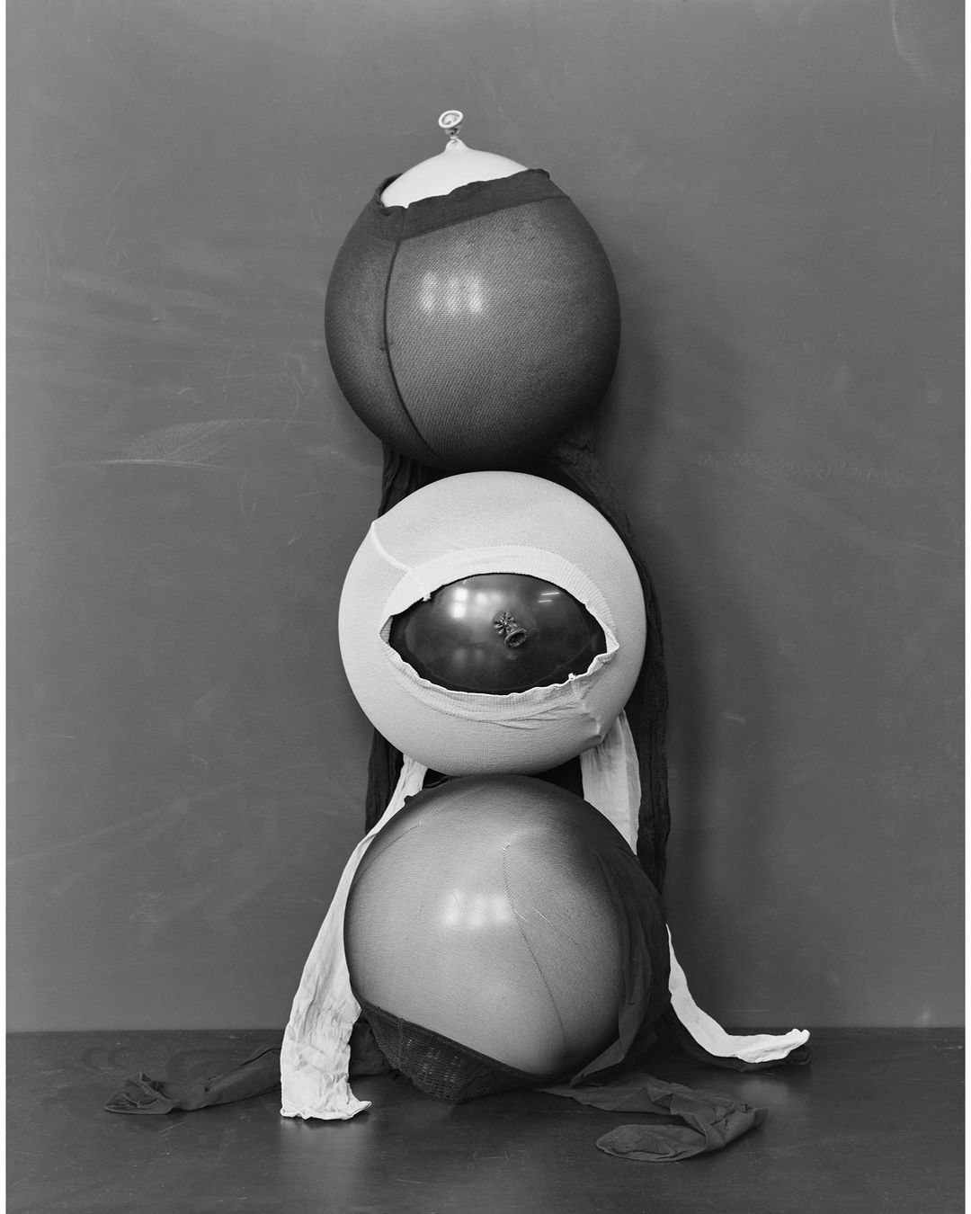 Monochrome studio shot featuring a sculptural arrangement of three spheres partially covered with sheer hosiery, creating a surreal, abstract composition.