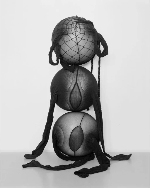 Monochrome image featuring three stacked spheres covered in black fishnet stockings against a gradient gray backdrop, creating an abstract visual.