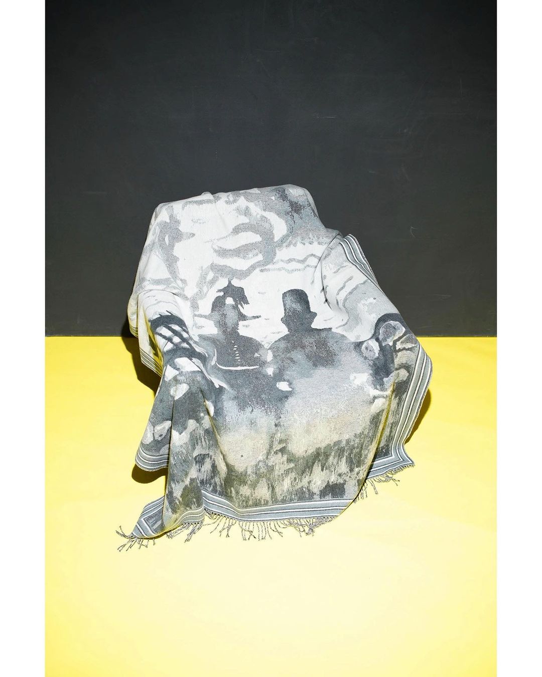 Printed scarf draped over an unseen object, featuring figures in a black-and-white vintage style, set against a yellow and black background.