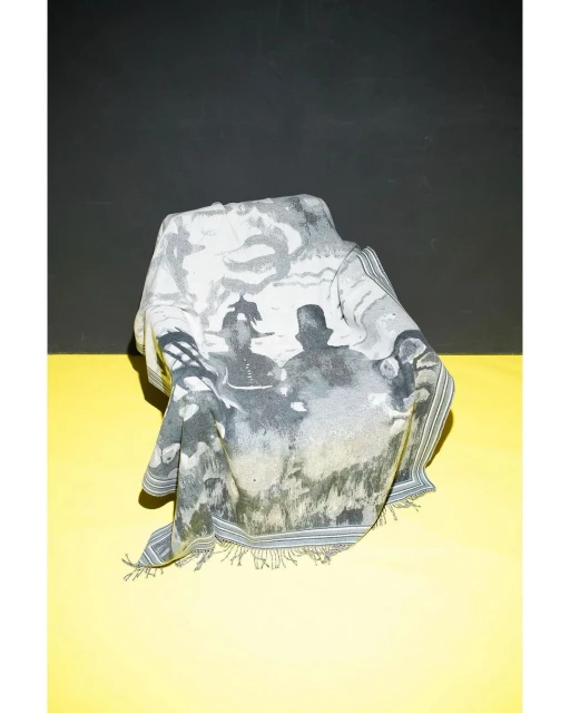 Printed scarf draped over an unseen object, featuring figures in a black-and-white vintage style, set against a yellow and black background.