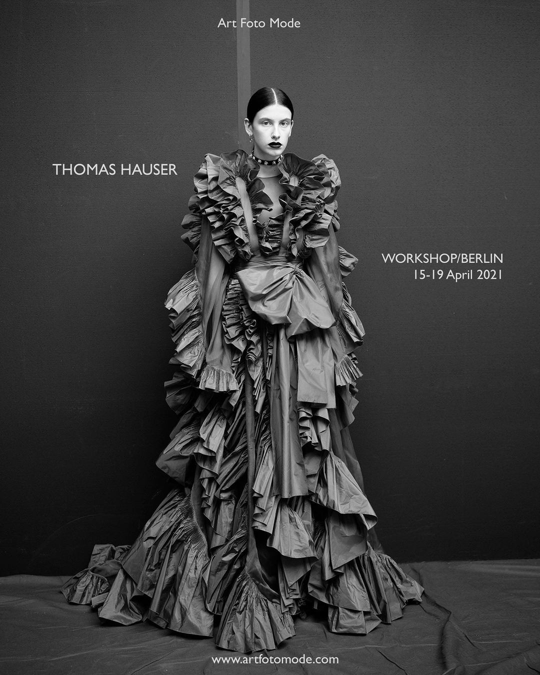 A striking black-and-white portrait showcases a model in a dramatically ruffled gown, complemented by dark makeup and a sleek, slicked-back hairstyle.