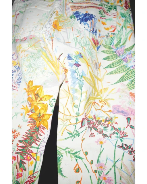 White jeans with a colorful floral pattern of yellow, blue, pink, and green flowers and foliage, creating a vibrant and artistic design.