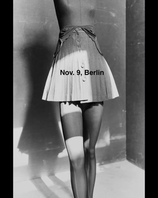 Black and white fashion shot: pleated skirt on a mannequin with fishnet stockings, in a studio with dramatic lighting.
