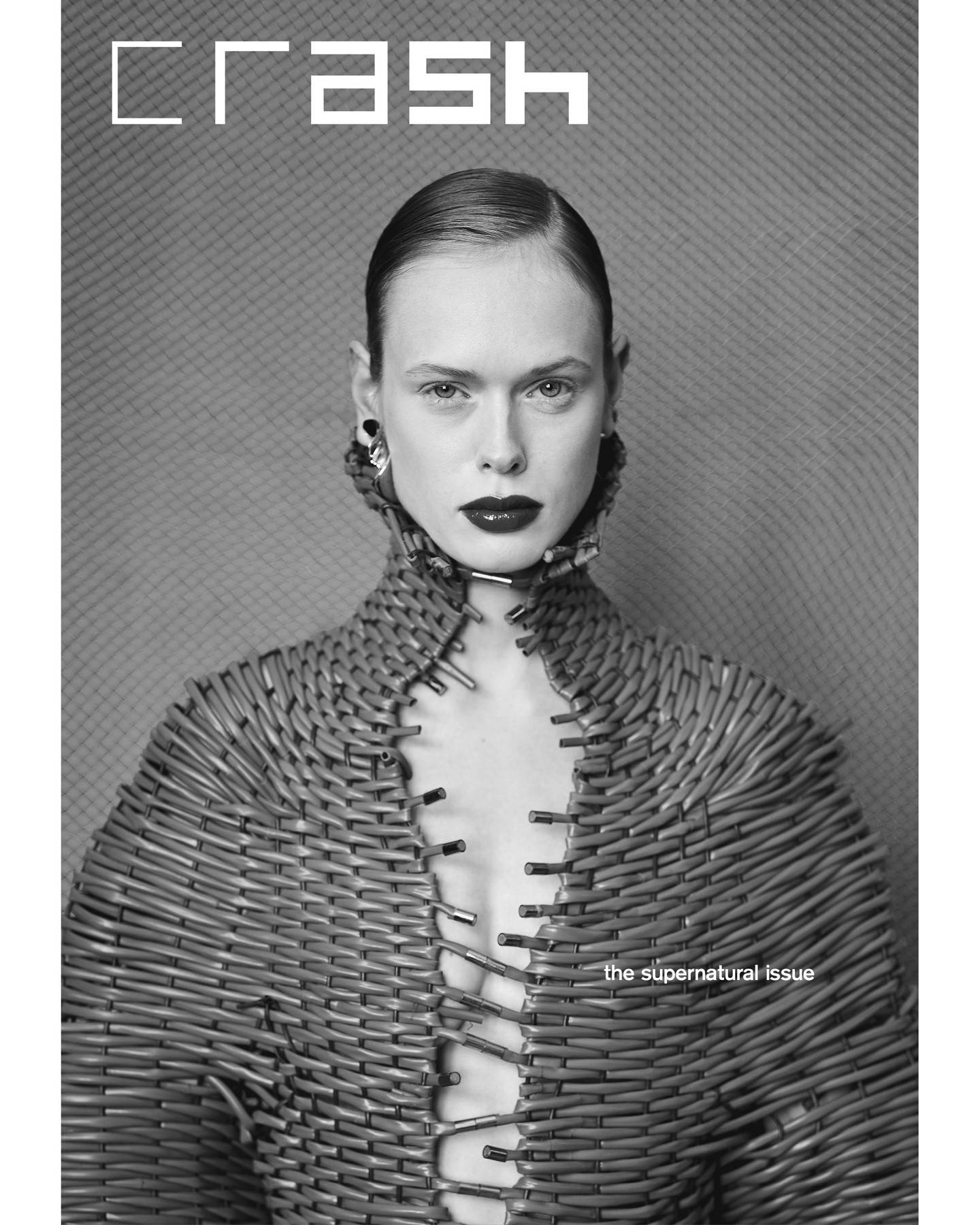 Monochrome portrait of a model wearing a textured wicker garment, silver earrings, and dark lipstick, posing for a 'Crash' magazine cover.