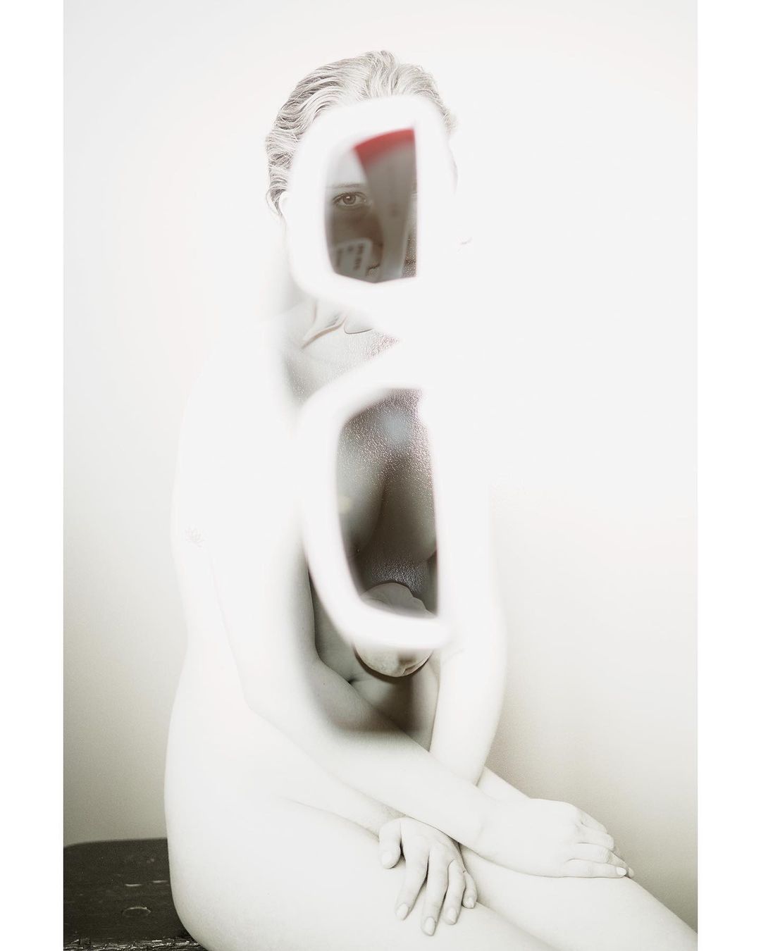 Abstract nude art photography featuring a woman with an obscured face in a blurred, desaturated style against a plain background.