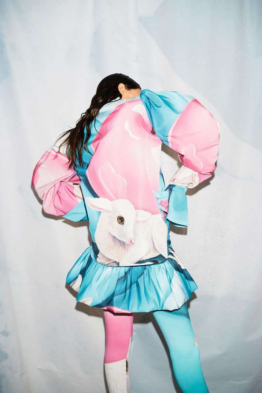 Model seen from behind wearing a colorful blue and pink dress with a painted white lamb graphic by Thomas Hauser in Paris.