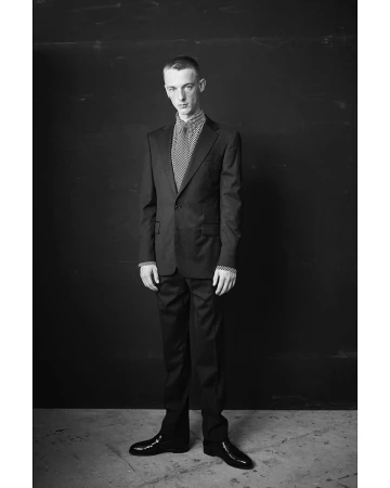 Portrait of a man in a dark suit standing against a dark wall by Thomas Hauser in Paris