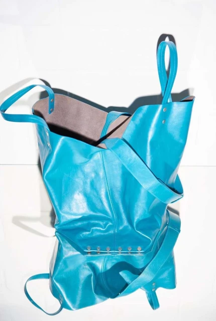 Stylish turquoise-blue leather tote bag is captured against a bright white background, with attention to its shape and material.