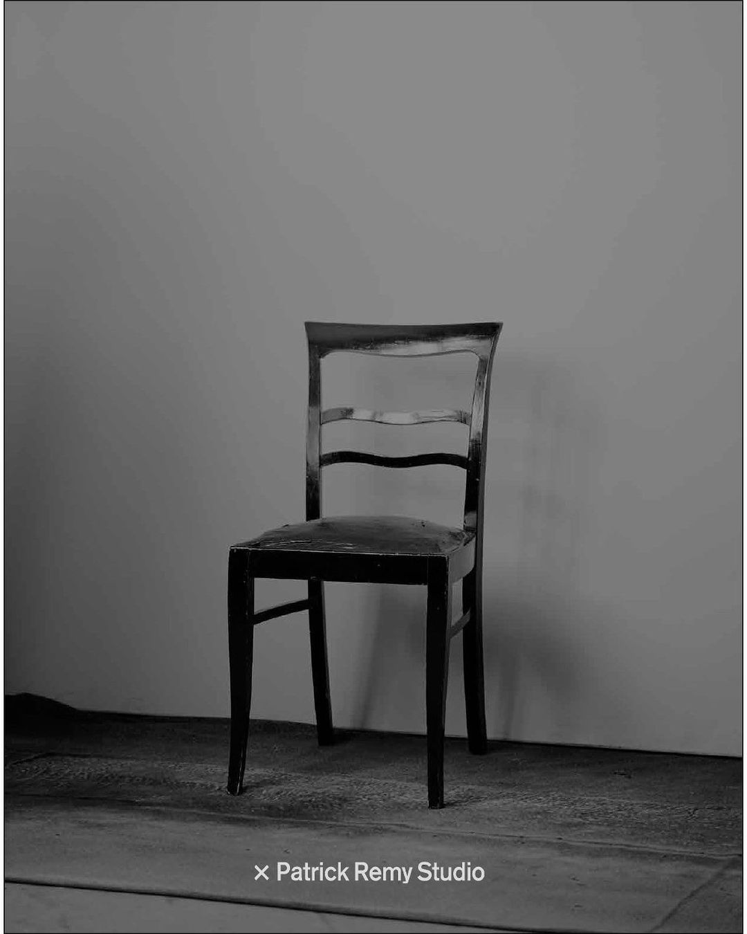 A black wooden chair positioned centrally against a neutral grey wall and studio floor by Thomas Hauser