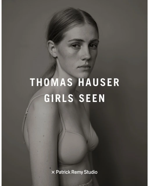 Black and white portrait of a young woman with blond hair looking at the camera, wearing a bra, posing in front of a grey background.