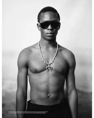 Black man wearing dark sunglasses and a pendant necklace in Paris, captured in a monochrome portrait by Thomas Hauser.