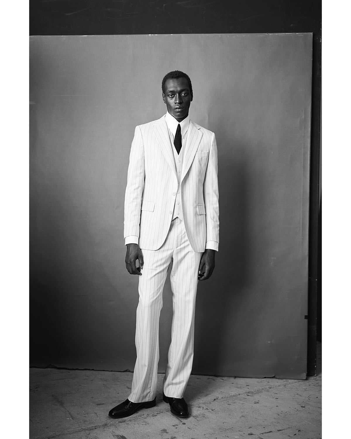 Black man wearing a pinstripe suit and tie standing against a studio backdrop, photographed in Paris by Thomas Hauser
