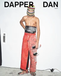 Man wearing a colorful knitted balaclava, red patterned trousers, and holding plastic water bottles in Paris by Thomas Hauser