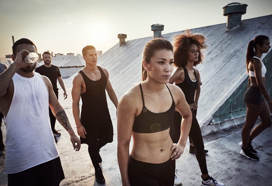 Group of diverse adult athletes in sportswear outdoors, posing against a cityscape background, bathed in soft, natural light during daytime.