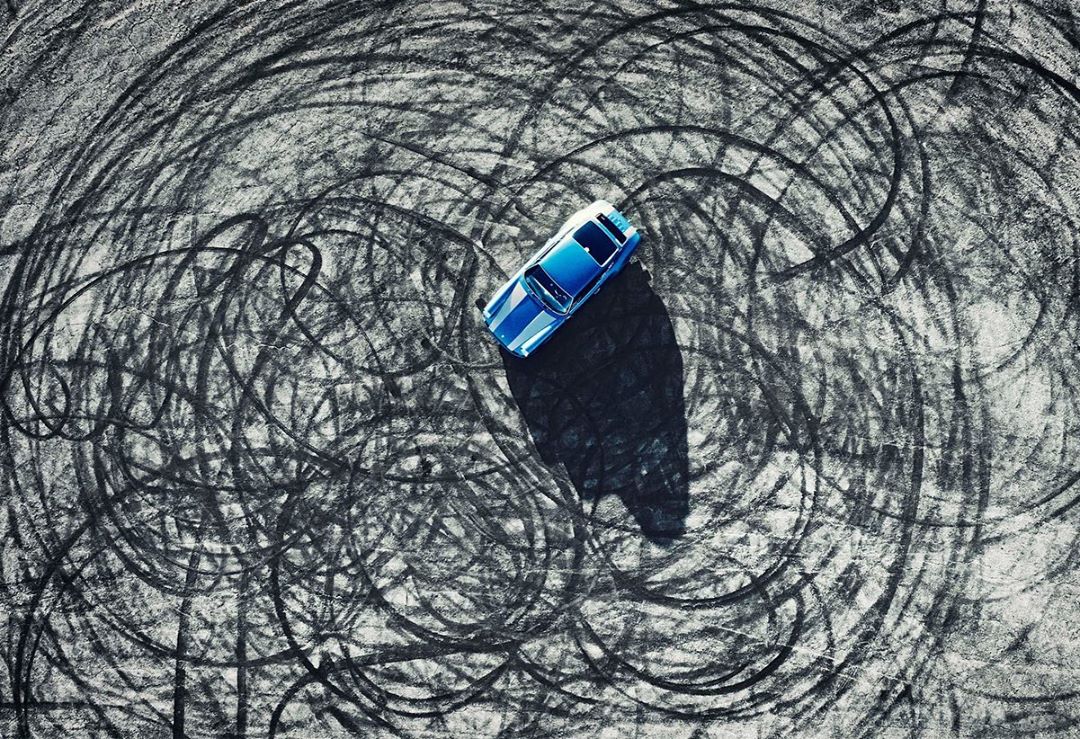 Aerial view of a blue convertible parked on asphalt covered with black tire tracks. Automotive and performance driving concept.