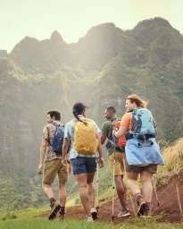 Four diverse hikers with backpacks walking up a mountain trail, photographed from behind by Thomas Hoeffgen.