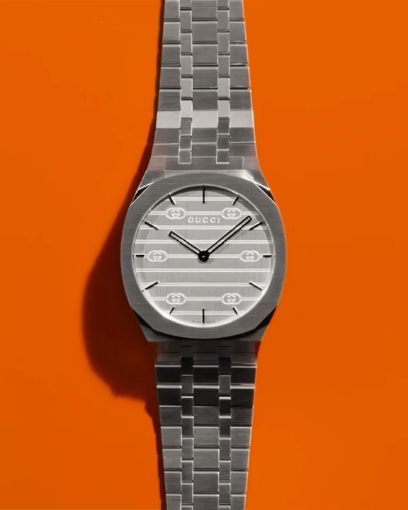 Luxury silver Gucci wristwatch with metal band on orange background. High-fashion product shot of expensive time-keeping accessory.