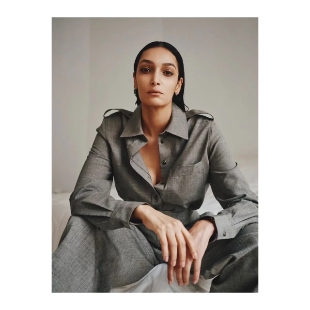 Portrait of woman in gray suit sitting indoors looking at the camera. The woman's gaze is direct and her expression is neutral.