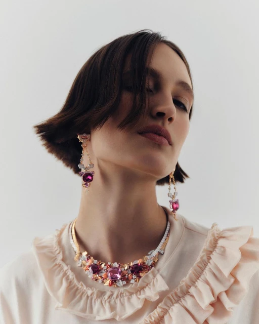A model wearing an elegant pink top and ornate jewelry in a studio setting, showcasing fashion and beauty with a soft, diffused light.