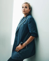 Blonde woman in a blue blazer leaning against a bright white wall, photographed by Thomas Laisne in Paris.