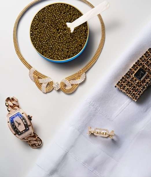 Luxury still life featuring a gold necklace with diamonds, caviar, gold bracelets and a gold ring on a white textured surface.