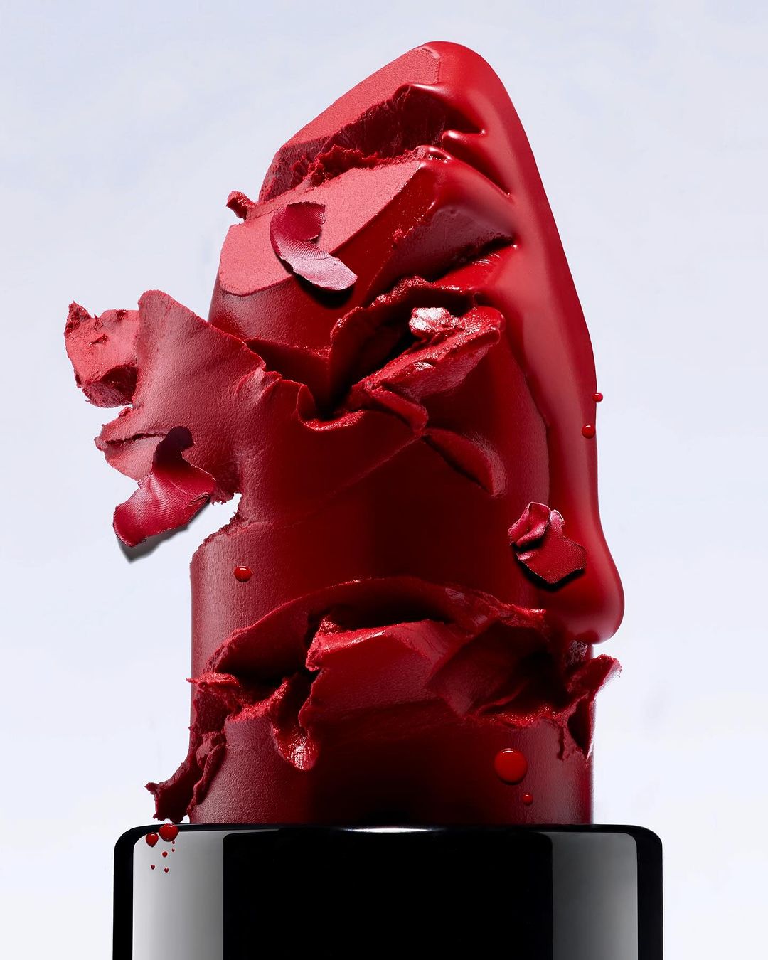 Close-up of broken red lipstick with a glossy finish against a gradient background in a beauty and cosmetics advertisement.
