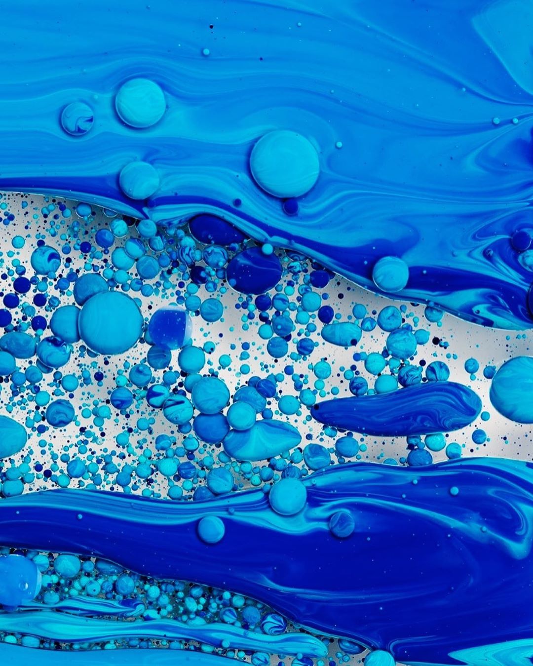 Macro photograph of blue and turquoise paint swirling and suspending in liquid, creating a textured, abstract pattern.