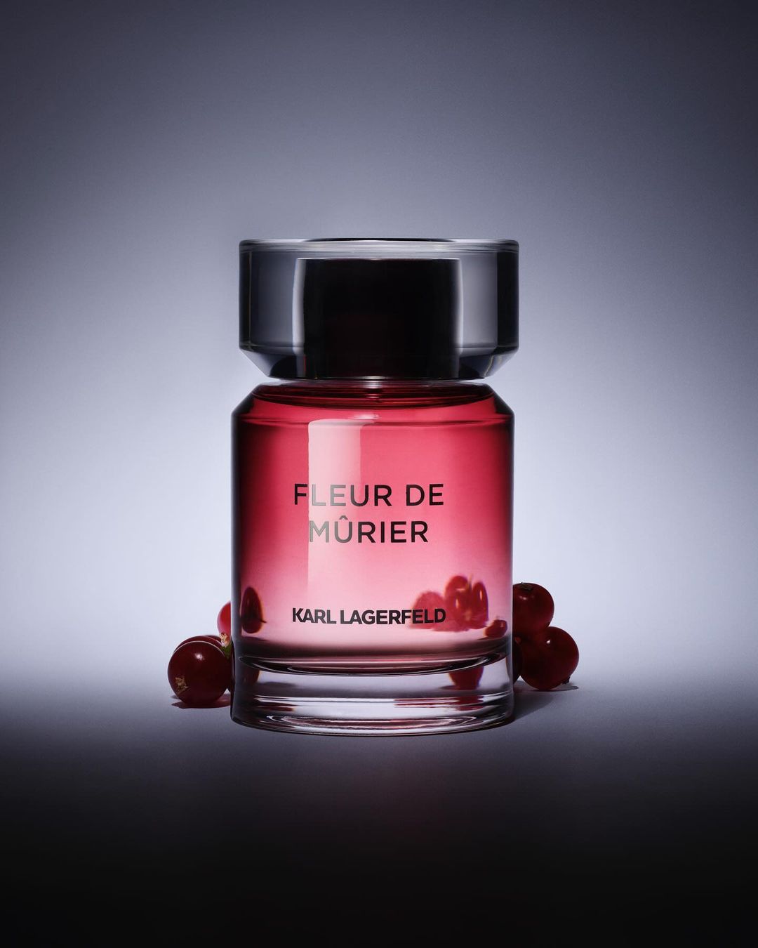 Karl Lagerfeld perfume bottle, Fleur de Mûrier, surrounded by red berries, against a gradient grey and white background.
