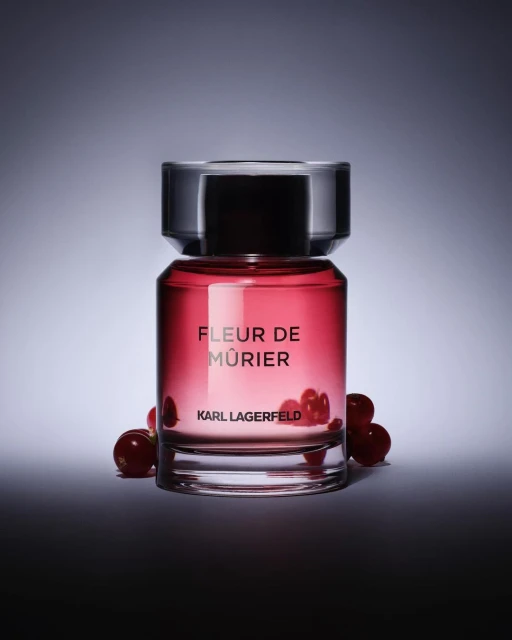 Karl Lagerfeld perfume bottle, Fleur de Mûrier, surrounded by red berries, against a gradient grey and white background.