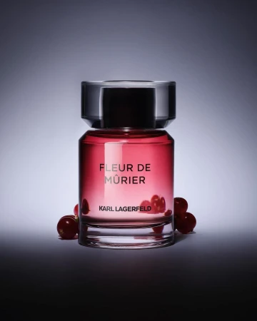 Karl Lagerfeld perfume bottle, Fleur de Mûrier, surrounded by red berries, against a gradient grey and white background.