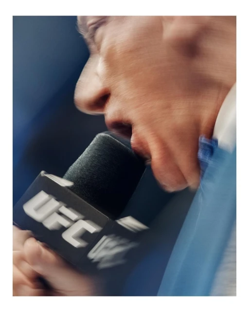 Close up of a person speaking into a microphone with the UFC logo, capturing a moment of communication and focus.