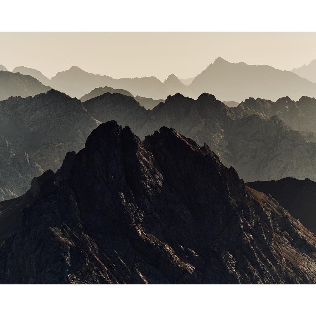 Scenic view of majestic, layered mountain range with rugged peaks, captured in a warm, hazy atmosphere highlighting the natural landscape.