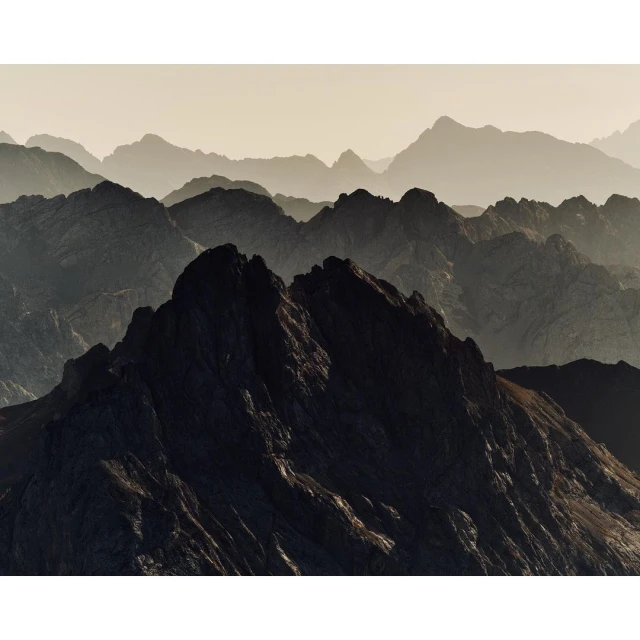 Scenic view of majestic, layered mountain range with rugged peaks, captured in a warm, hazy atmosphere highlighting the natural landscape.