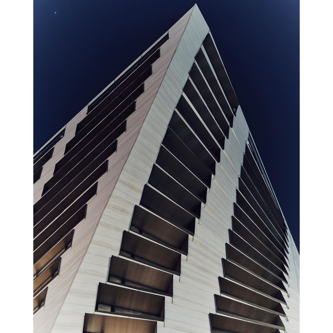 Low-angle view of a tall, modern skyscraper with a textured facade and recessed windows against a dark blue, twilight sky. 