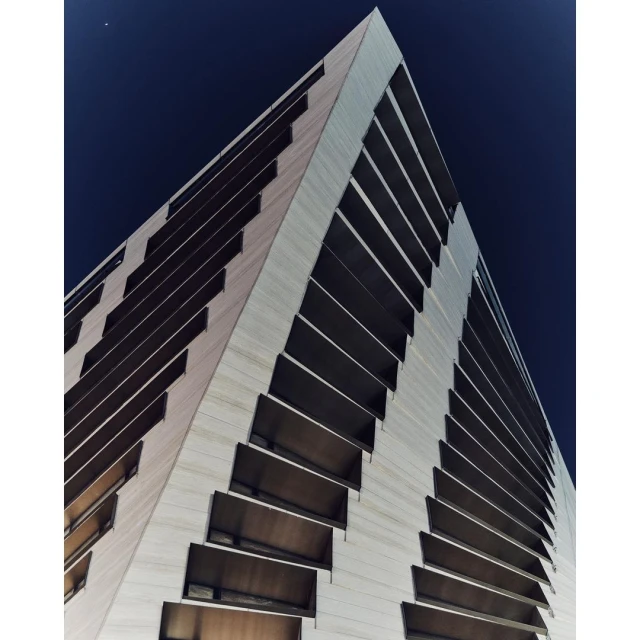 Low-angle view of a tall, modern skyscraper with a textured facade and recessed windows against a dark blue, twilight sky. 