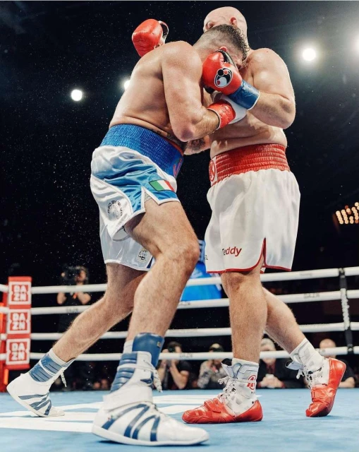 Two boxers in a close match, facing each other inside a boxing ring, wearing boxing gloves and shorts. Intense moment of the fight.