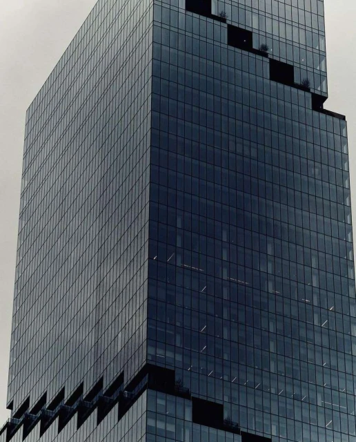 Exterior close-up of a modern, high-rise glass skyscraper with a grid-like pattern of windows against a cloudy sky in an urban setting.