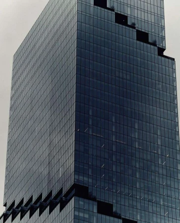 Exterior close-up of a modern, high-rise glass skyscraper with a grid-like pattern of windows against a cloudy sky in an urban setting.