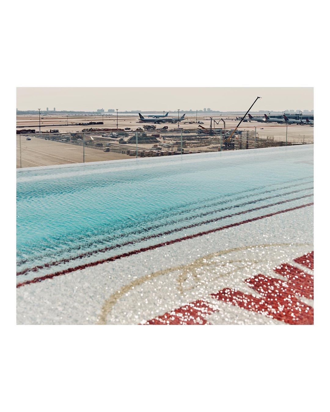 Airport runway and airplanes are visible beyond a swimming pool with decorative tiles in the foreground, shot in daytime.