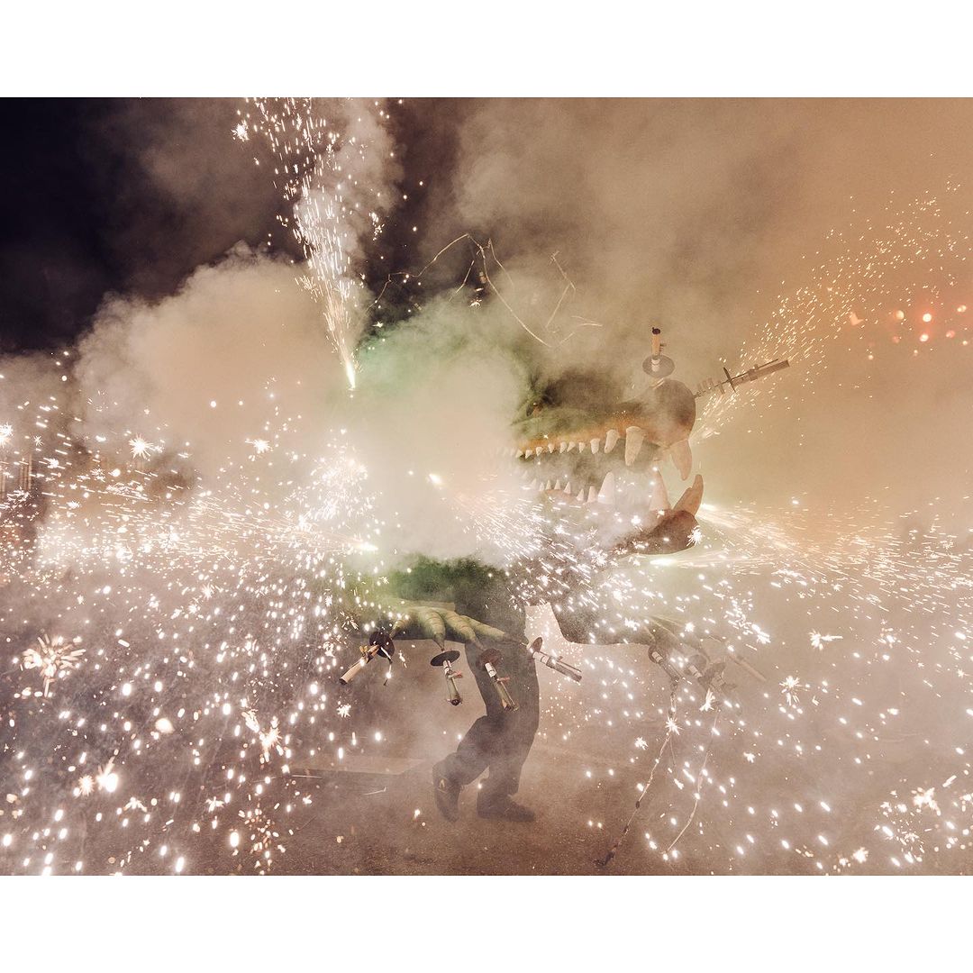 Person in a large dragon costume surrounded by smoke and fireworks at night, low angle, event photography.