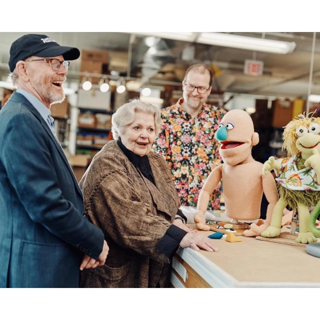 Group of people with puppets in an indoor space, featuring adults, puppets with distinct facial expressions, and a well-lit environment.
